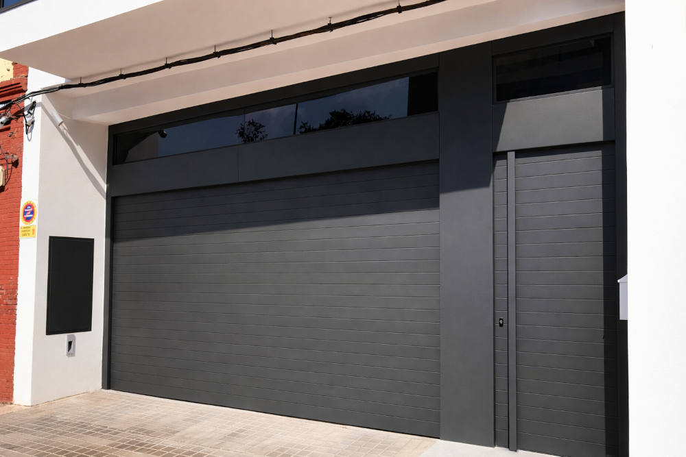Puerta de garaje seccional gris antracita con puerta peatonal integrada en Vilagarcía de Arousa Puerta de garaje seccional gris antracita con puerta peatonal integrada instalada en Vilagarcía de Arousa
